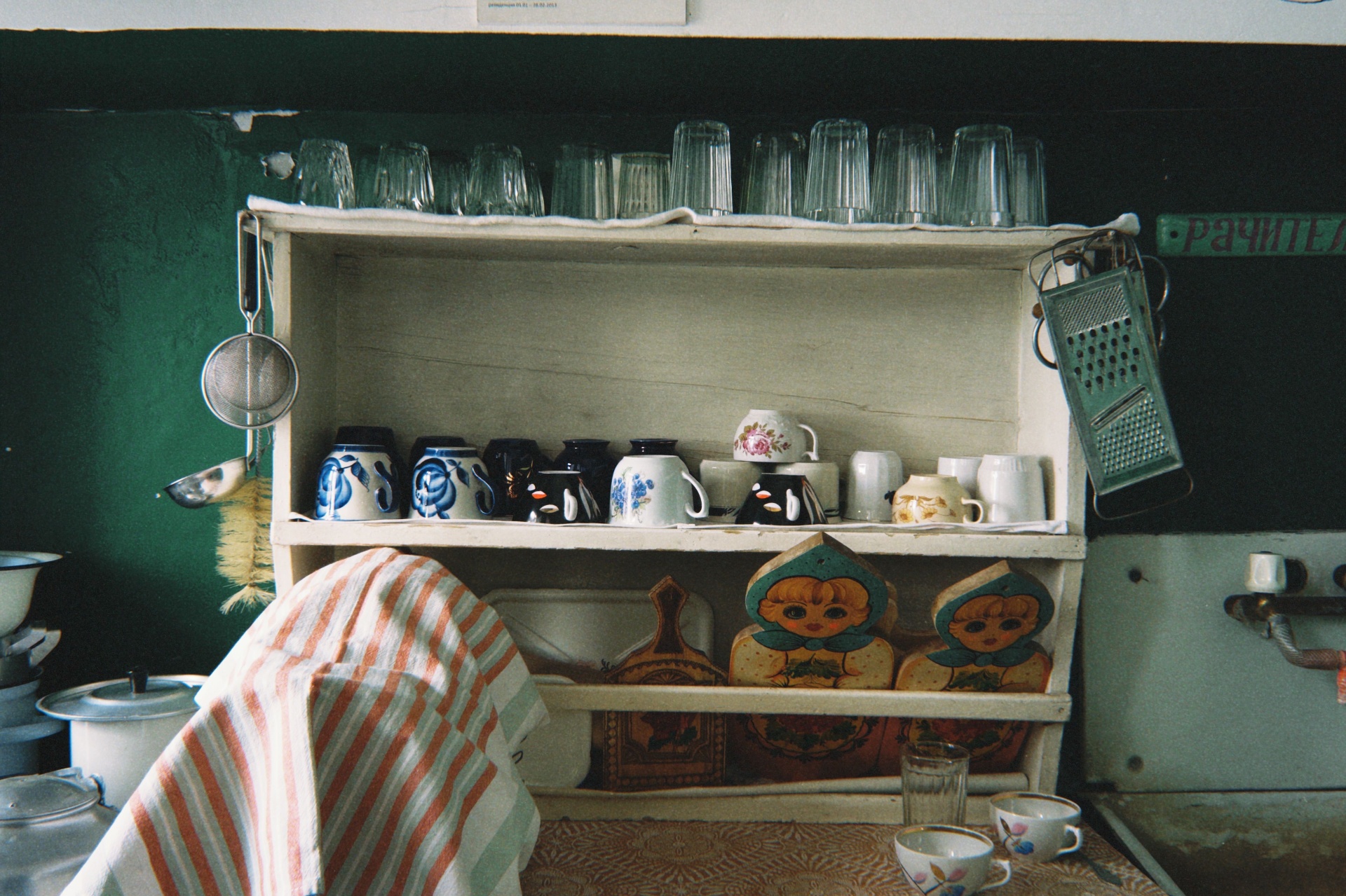 a vintage green-walled kitchen shelf, mugs and glassware caught in soft afternoon light